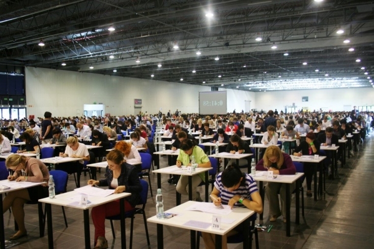 uczestnicy egzaminu siedzą przy pojedynczych stolikach w dużej hali